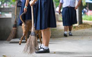 las alumnas ayudan a barrer el suelo de hormigón con una escoba mientras el perro camina. foto