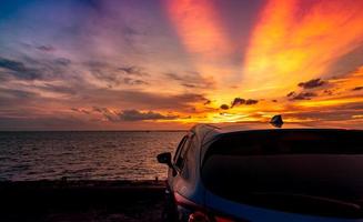 Rear view blue compact SUV car with sport and modern design parked on concrete road by the sea at sunset. Electric car technology and business. Hybrid auto and automotive. Tropical road trip travel. photo