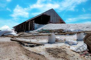 granero con salmuera en saco. montón de sal marina orgánica y cesta de bambú frente al granero con cielo azul y nubes blancas en verano. materia prima de sal industrial. sal marina en saco de plástico. foto