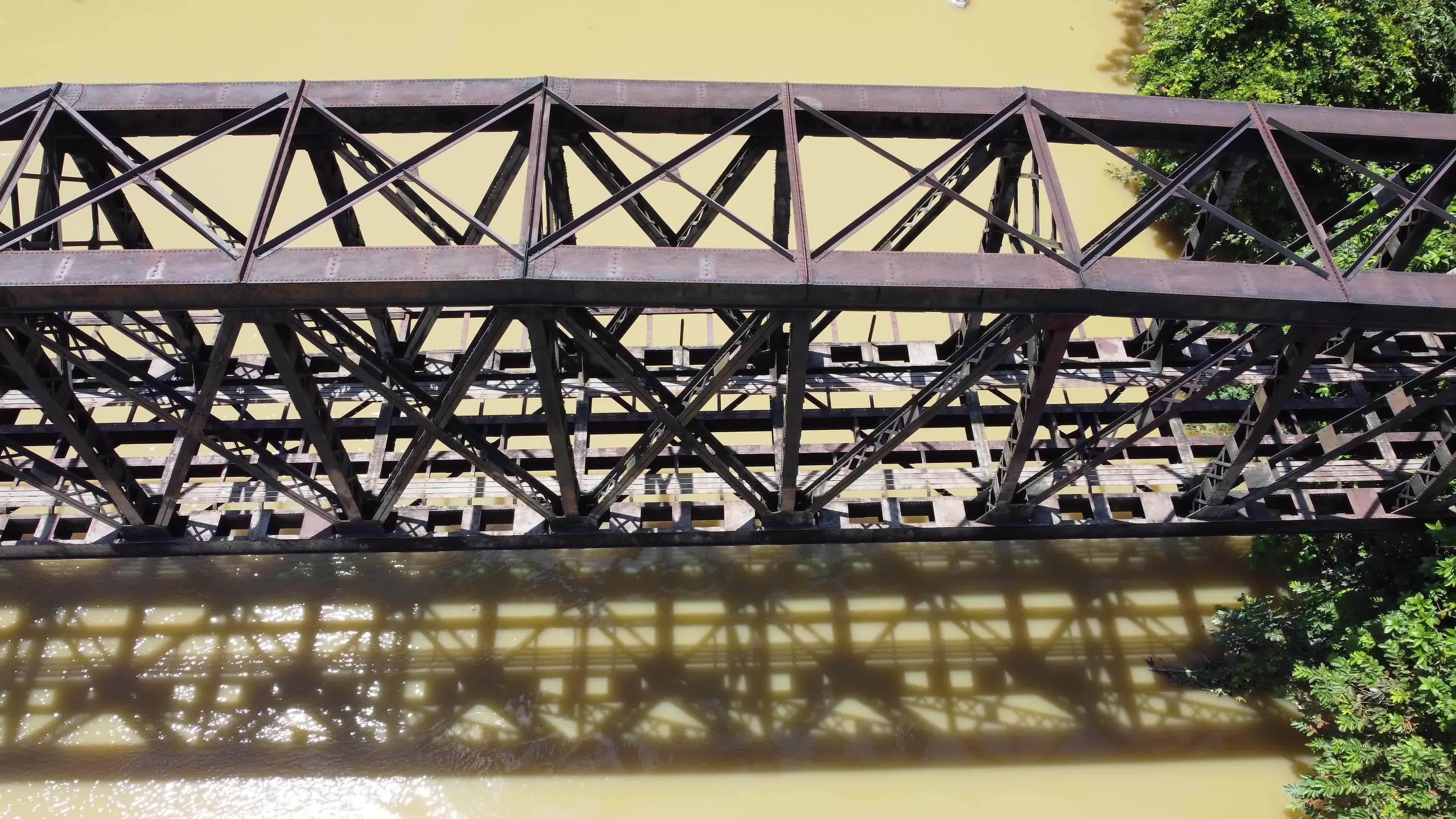 Aerial dolly move left and look down steel railway bridge at river