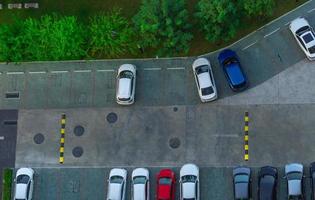 Above view of cars parked at car parking area of the apartment. Aerial view concrete car parking lot with speed bump near green trees in the park. Outdoor car parking space with empty slots. photo