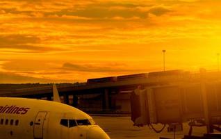 Commercial airplane parked at jet bridge for passenger take off at the airport. Aircraft passenger boarding bridge docked with golden sunset sky near road. Departure flight of international airline. photo