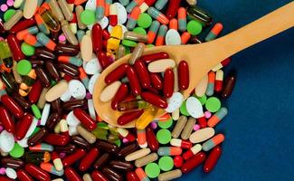 Pile of colorful tablets and capsules pills and wood spoon on blue background. Antibiotic resistance concept. Pharmaceutical industry. Global healthcare. Drug interactions concept photo