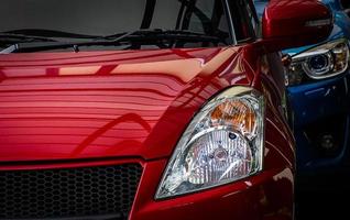 Close up headlamp light of red shiny SUV car parked on concrete parking lot of the hotel or shopping mall. Automotive industry concept. Electric or hybrid car technology. Car rental and dealership. photo