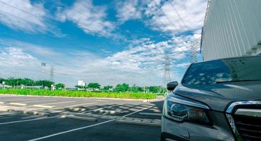 vista frontal del automóvil estacionado en el estacionamiento. área de estacionamiento al aire libre del centro comercial con línea de cable eléctrico y torre eléctrica de alto voltaje como fondo. estacionamiento de asfalto contra el cielo azul. foto