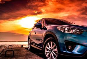 camión suv compacto azul con diseño deportivo, moderno y de lujo estacionado en una carretera de hormigón junto al mar al atardecer. vista frontal del hermoso coche híbrido. conduciendo con confianza. viajar de vacaciones en la playa. foto