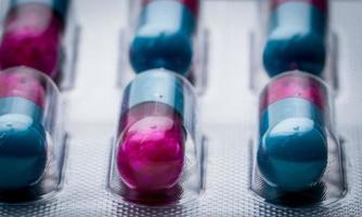 Selective focus of blue, pink capsule with granule in side pills. Pills in blister pack. Pharmaceutical dosage form and packaging. Itraconazole 100 mg  Anti fungal medicine. photo