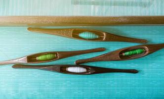 Top view of yarn in weaving shuttle tool on weaving machine. Textile fabric weave. Weaving using traditional weaving loom and shuttle. Textile or cloth production in Thailand. Green handmade cloth. photo