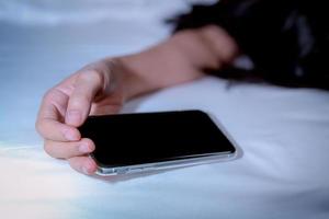 Asian woman sleeping in bed at home and hand holding mobile phone. Woman using smartphone in bedroom. Young woman addicted using smartphone. Texting on cellphone with tired until falling asleep. photo