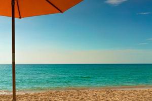 Orange beach umbrella on golden sand beach by the sea with emerald green sea water and blue sky and white clouds. Summer vacation on tropical paradise beach concept. Skyline between sea and sky. photo