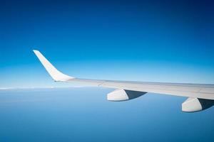 Wing of plane over white clouds. Airplane flying on blue sky. Scenic view from airplane window. Commercial airline flight. Plane wing above clouds. Flight mechanics concept. International flight. photo