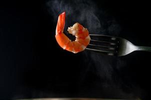 camarones al vapor en tenedor aislado sobre fondo oscuro con espacio de copia. buffet de mariscos en concepto de restaurante. uso para publicidad de promociones de buffet de mariscos foto