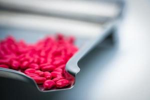 Macro shot detail of red kidney shape sugar coated tablet pills on stainless steel drug tray