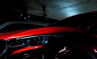 Closeup headlight of shiny red luxury SUV compact car parked in shopping mall underground parking lot. Elegant electric car technology and business concept. Hybrid auto and automotive concept. photo