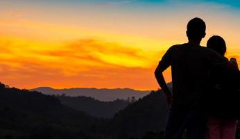 vista trasera de una pareja romántica viendo la hermosa puesta de sol sobre la capa montañosa. viaje en pareja. mochilero feliz enamorado y viajando luna de miel. silueta de dos turistas que van de excursión a la cima de la montaña. foto