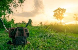 Shoulder type grass cutting machine. Lawn mower engine. Weed and grass mowing with petrol lawn mower in the morning with sunrise sky at rice farm. Cutting green grass for feed livestock in Thailand. photo