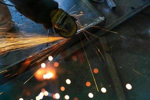 Industrial worker using angle grinder grinding metal on welding seams. Worker working with angle grinder and has sparks. Tool for cut steel. Safety in industrial workplace. Metal factory industry. photo