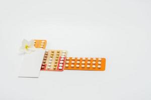 Birth control pills or contraceptive pill with paper case and white flower on white background. Family planning concept. Hormone replacement therapy. Hormonal acne treatment with anti-androgenic pill. photo