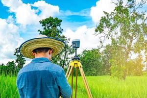 ingeniero o topógrafo inteligente asiático que trabaja en la pantalla del controlador para inspeccionar la tierra en el campo de arroz, tailandia. instrumento topográfico gps. equipo gps estudio de la tierra para el mapa. la gente trabaja en buen ambiente. foto