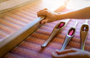 Woman working on weaving machine for weave handmade fabric. Textile weaving. Weaving using traditional hand weaving loom on cotton strands. Textile or cloth production in Thailand. Asian culture. photo