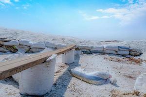 Brine salt farm with blue sky and white clouds. Pile of organic sea salt near warehouse. Raw material of salt industrial. Ocean salt. Summer travel in Thailand concept. Sodium chloride mineral. photo