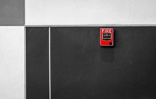 Fire alarm on black and white concrete wall. Warning and security system. Emergency equipment for safety alert. Red box of fire alarm on wall of school, hospital, factory, office, apartment, or home. photo