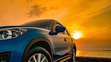 Blue compact SUV car with sport and modern design parked on concrete road by the sea at sunset. Environmentally friendly technology. Business success concept. photo