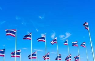 muchos de la bandera de tailandia ondeando en la parte superior del asta de la bandera contra el cielo azul. la bandera tailandesa se dibujó en la parte superior del asta de la bandera. tela rectangular de color rojo, azul y blanco. bandera nacional del reino de tailandia. foto