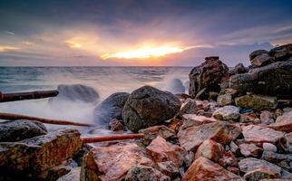 Ocean water splash on rock beach with beautiful sunset sky and clouds. Sea wave splashing on stone at sea shore on summer. Nature landscape. Tropical paradise beach at sunset. Rock beach at coast. photo