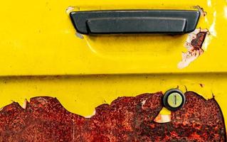 Close up old car door with rusty. Abandoned rusty yellow car with black handle. Car coloring is peeling. Old and rusted automobile door texture background. Cracked paint. Hole of auto key. photo