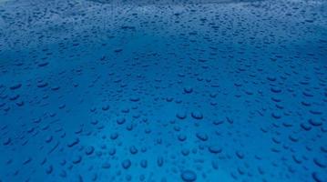 Water drop splash on clean blue texture with nature pattern. Raindrops on blue surface of car hood. Water droplets on blue background. Close-up rain drop on blue car. Refreshing and aqua concept. photo