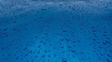 Water drop splash on clean blue texture with nature pattern. Raindrops on blue surface of car hood. Water droplets on blue background. Close-up rain drop on blue car. Refreshing and aqua concept. photo