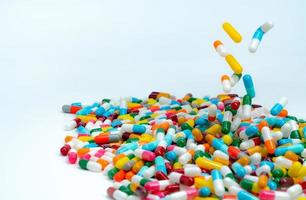 Selective focus on pile of antibiotic capsule pills. Colorful antibiotic capsules pill falling on white table. Antibiotic drug resistance concept. Antimicrobial drug overuse. Pharmaceutical industry. photo