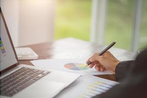 Hand of businessman writing on paper in office, graphs showing the results of their successful teamwork, photo