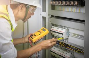 Los ingenieros eléctricos prueban el voltaje y la corriente de los cables en el control del gabinete eléctrico. El multímetro está en manos de los detalles del electricista. foto