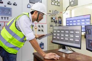 Experienced electrician working in a power plant control room. Engineer working in electric power distribution substation checking status. Machine operation data. photo