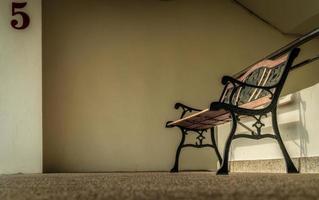 Empty wrought iron bench placed near stairs of the building. Depressed, sad and lonely concept. One empty wrought iron bench. Single bench at apartment building. Lonely concept. photo