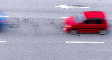 coche rojo y azul moviéndose rápidamente en la carretera de asfalto en la ciudad. movimiento borroso del coche compacto de alta velocidad en la carretera asfaltada. transporte urbano con concepto de hora punta. viajar en automóvil. concepto de consumo de combustible del automóvil. foto