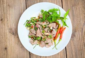 Pork liver salad with fresh chili herbs, spices, Spicy liver salad on white plate wooden table background, Thai food photo