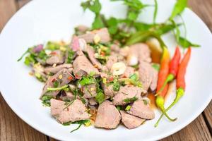 Spicy liver salad on white plate wooden table background, Pork liver salad with fresh chili herbs, spices, Thai food photo