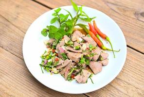 Spicy liver salad on white plate wooden table background, Pork liver salad with fresh chili herbs, spices, Thai food photo