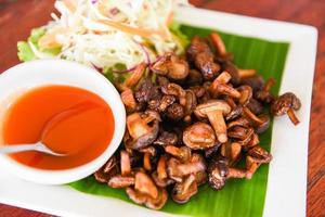 Delicious fried mushrooms in plate on wooden table, top view - cooked shiitake mushrooms fried with tomato sauce and vegetables photo