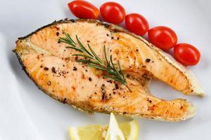 Salmon steak with herbs and spices rosemary lemon tomato on plate background - Close up cooked salmon fish fillet steak seafood photo