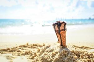 Ice cream cone on sand beach background - Melting ice cream on beach sea in summer hot weather ocean landscape nature outdoor vacation , ice cream chocolate photo