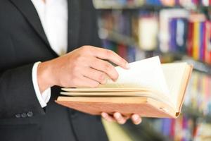 hombre de negocios o estudiante sosteniendo un libro a mano - concepto de estudio de educación empresarial hombre leyendo un libro con estantería en el fondo de la biblioteca foto