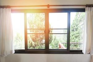ventana del dormitorio por la mañana - luz del sol a través de cortinas abiertas en la habitación con balcón y árbol natural en la ventana exterior foto