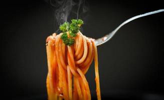 espaguetis a la boloñesa pasta italiana con perejil en el restaurante comida italiana y concepto de menú - espaguetis en tenedor y fondo negro foto