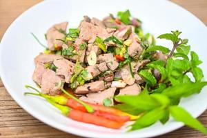 Spicy liver salad on white plate wooden table background, Pork liver salad with fresh chili herbs, spices, Thai food photo