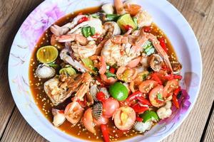 ensalada picante mariscos en bandeja, ensalada cocina tailandesa deliciosos mariscos picantes con cangrejo camarones berberechos calamares y especias ingrediente limón lima tomate chile fresco comida picante foto