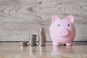 apilar monedas y alcancía sobre fondo de madera, alcancía rosa ahorrando dinero para estudio educativo o concepto de inversión foto